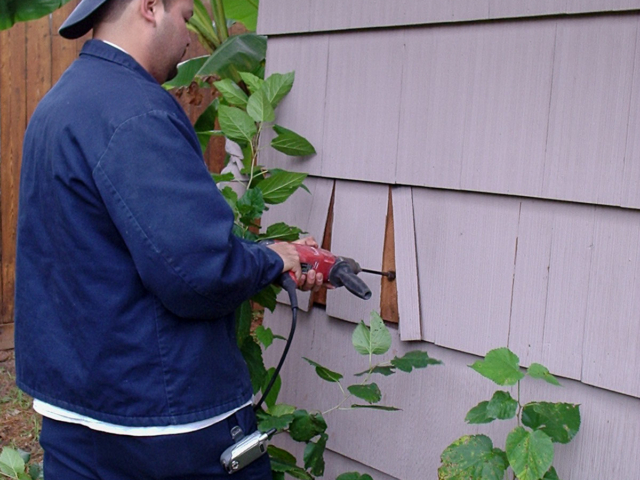 Man Pressure Filling Walls with Cellulose Insulation from Outside of House with Cedar Shake Siding